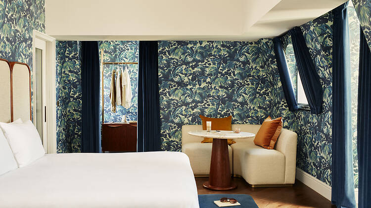 A bed against a decorated blue wall covered in patterns, with a sofa to the right and clothes on a hanger in the background