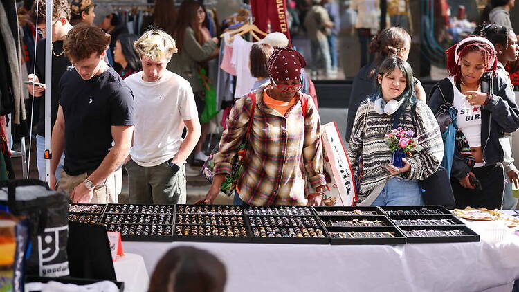 A wide shot of people browsing jewelry at an outdoor market. A wide shot of people browsing jewelry at an outdoor market.