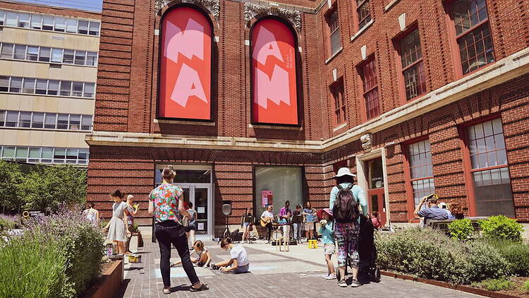 A wide shot of people gathering outside a museum entrance courtyard. A wide shot of people gathering outside a museum entrance courtyard.