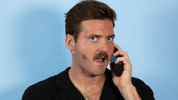 Close-up of a person talking on a phone against a blue background.
