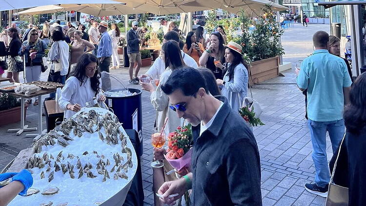 A wide shot of people enjoying drinks and oysters at an outdoor plaza. A wide shot of people enjoying drinks and oysters at an outdoor plaza.
