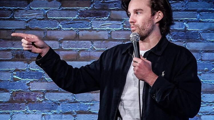 Close-up of a comedian performing with a microphone on a brick stage.