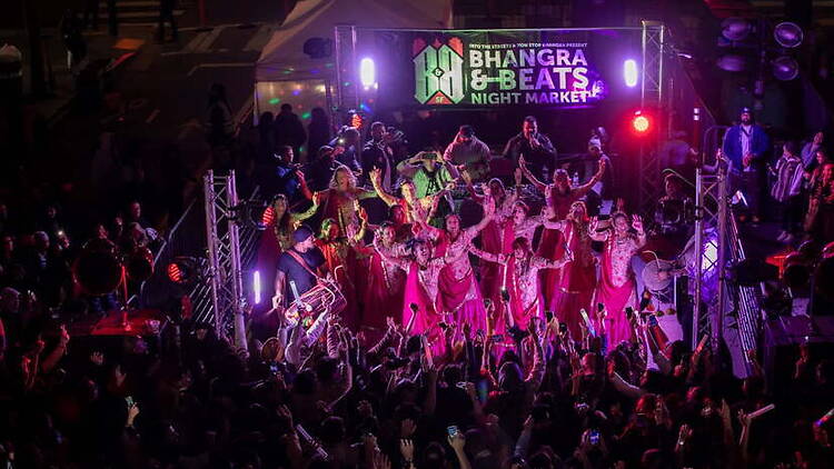 A wide shot of dancers performing at a crowded night market stage. A wide shot of dancers performing at a crowded night market stage.
