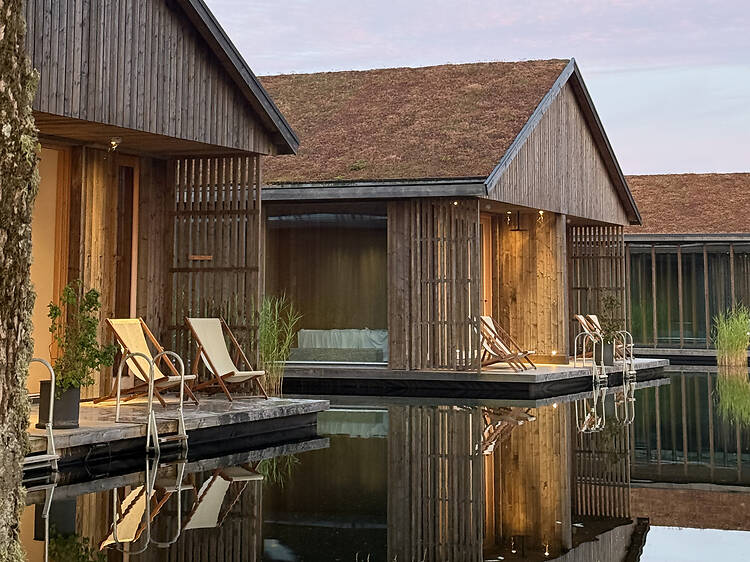 Ästad Vingård, destinationshotell Modern wooden cabins at the luxury hotel Ästad Vingård with green living roofs and deck chairs overlooking a calm pool with clear reflections.