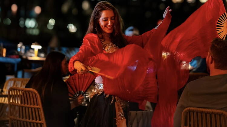 A close-up of a dancer performing with red veils at an outdoor event. A close-up of a dancer performing with red veils at an outdoor event.