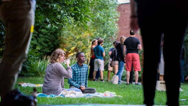 A wide shot of people sitting and socializing on a lawn in a museum courtyard A wide shot of people sitting and socializing on a lawn in a museum courtyard