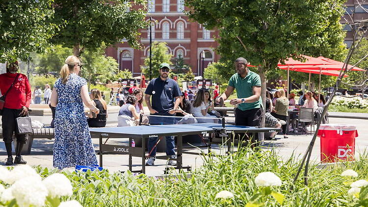 Wide view of people playing table tennis in a public park. Wide view of people playing table tennis in a public park.