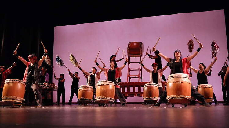 A wide shot of drummers performing on stage during a taiko drum performance. A wide shot of drummers performing on stage during a taiko drum performance.
