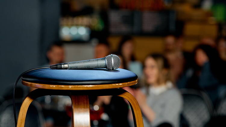 A close-up of a microphone on a stool in a comedy venue. A close-up of a microphone on a stool in a comedy venue.
