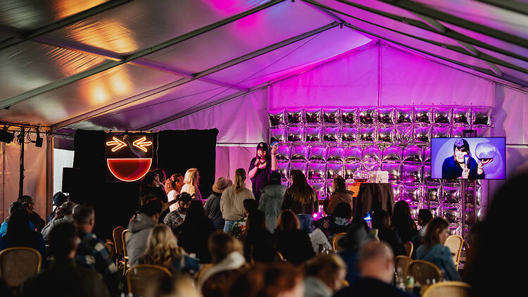 Comedy in the Vines people under a tent with purple lighting
