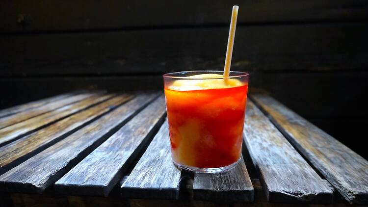 A redish and mango cocktail on a wooden tabel