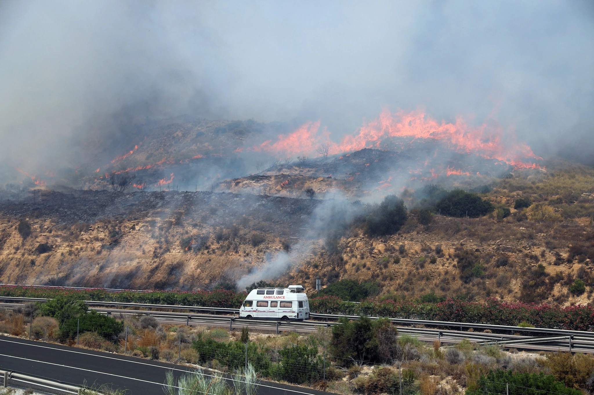 An ambulance drives urgently along a highway as a fast moving wildfire approaches