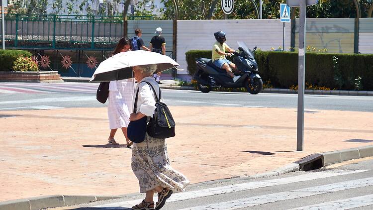 An elderly woman walks across the intersection with a parasol to protect herself from the heat An elderly woman walks across the intersection with a parasol to protect herself from the heat