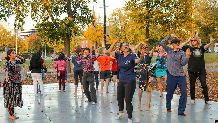 A wide shot of people dancing together on an outdoor plaza in a park. A wide shot of people dancing together on an outdoor plaza in a park.