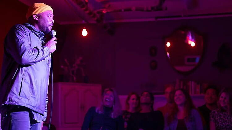 A wide shot of a comedian performing on stage in front of a laughing audience at a comedy club. A wide shot of a comedian performing on stage in front of a laughing audience at a comedy club.