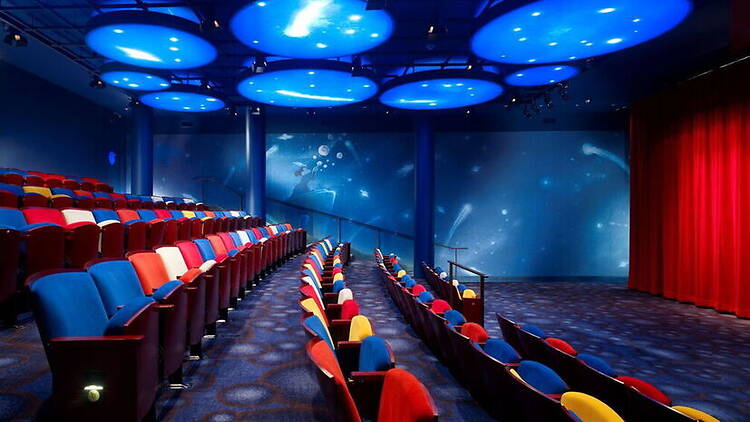 A wide shot of colorful theater seats facing a stage in an auditorium. A wide shot of colorful theater seats facing a stage in an auditorium.