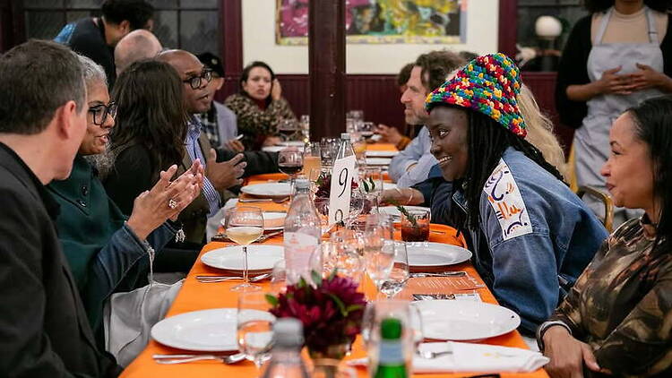 A wide shot of people dining and talking around a long table in a restaurant.