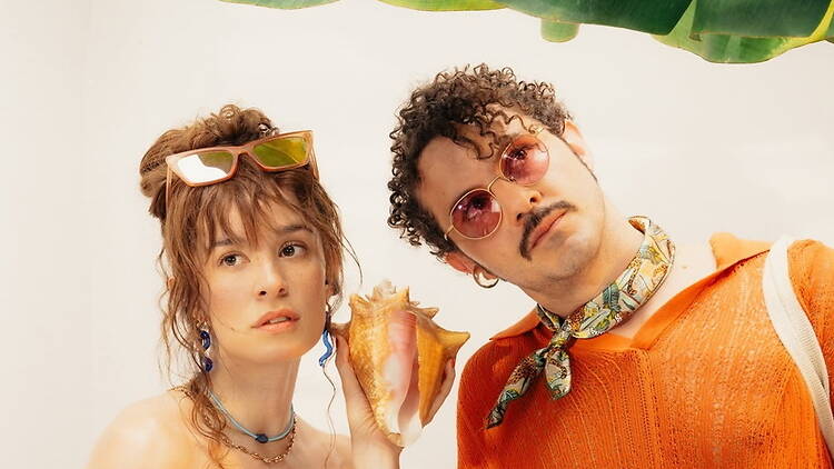 A close-up of two people posing with a seashell against a bright backdrop. A close-up of two people posing with a seashell against a bright backdrop.