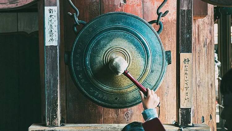 A close-up of a person using a mallet to ring a temple bell. A close-up of a person using a mallet to ring a temple bell.