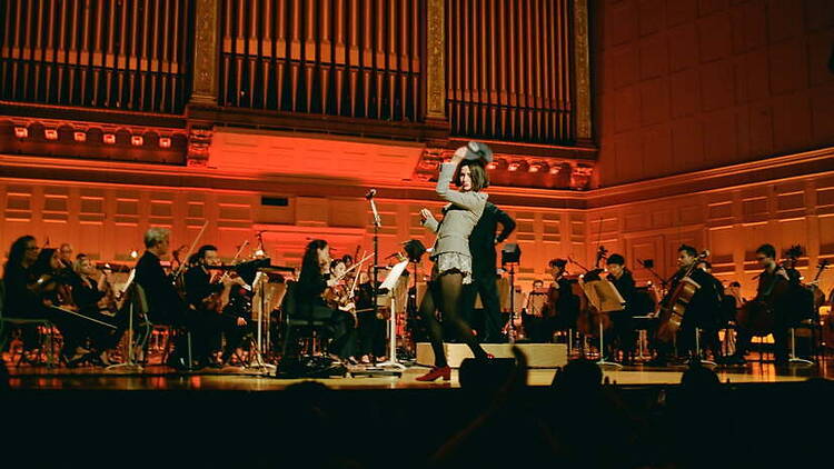 Wide view of orchestra and performer performing onstage in a concert hall.