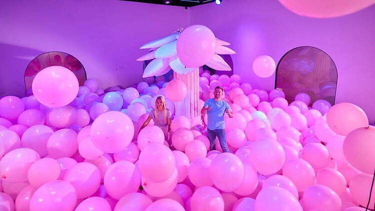 A wide shot of people playing in a balloon-filled room at an indoor event