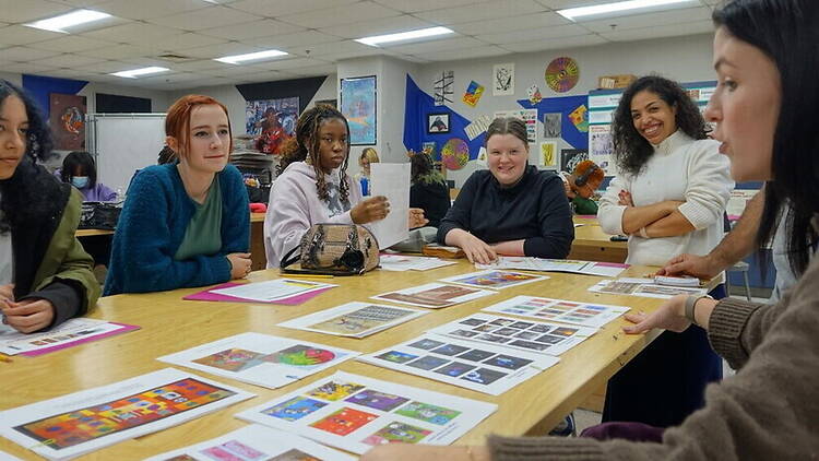 A wide shot of students discussing artwork with an instructor in a classroom