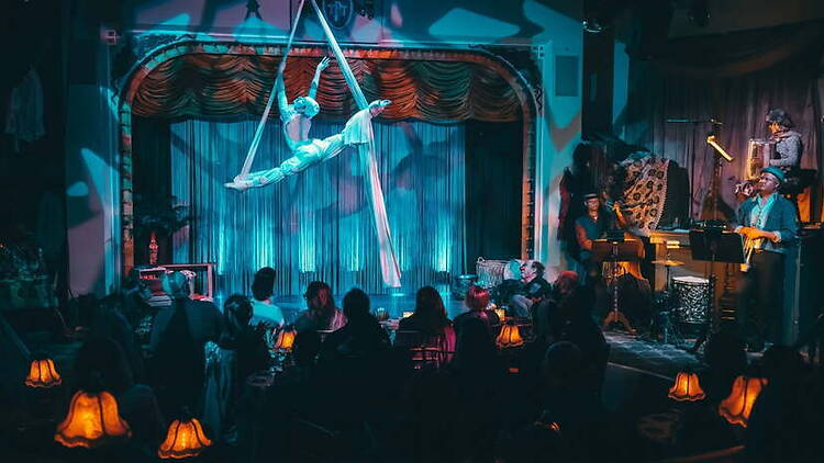 Wide view of aerial performer performing above an audience in a theater.