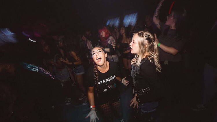 A wide shot of people dancing together at a live music event in a dark indoor venue. A wide shot of people dancing together at a live music event in a dark indoor venue.