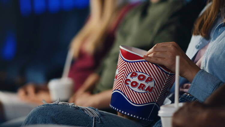 Close-up of person holding popcorn while watching a movie in a theater.