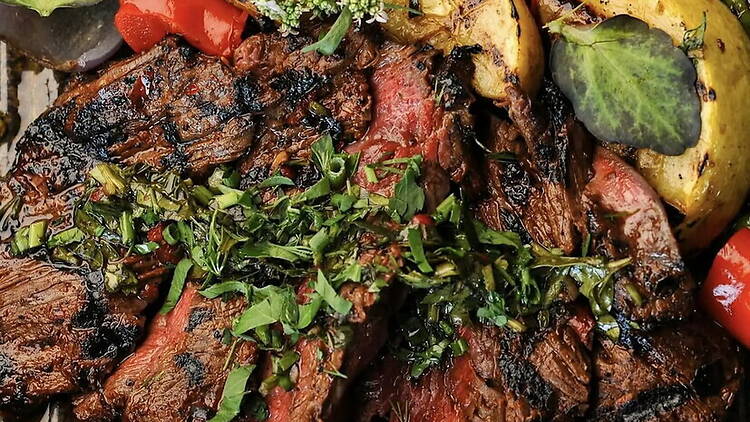 A close-up of grilled steak with herbs and roasted vegetables on a serving platter.