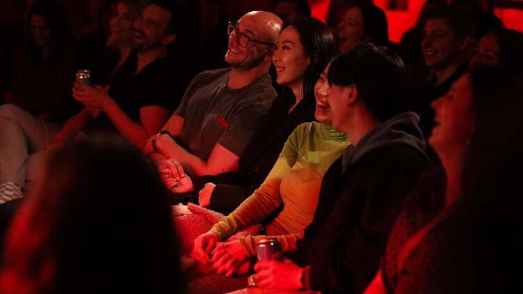 A wide shot of people laughing during a live comedy show in an indoor venue.