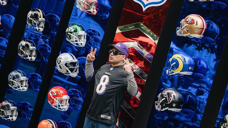 Man poses with NFL team helmets on display.