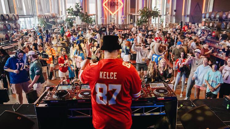 DJ wearing a Travis Kelce jersey in front of crowds.