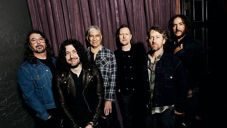 A wide shot of six band members posing in front of purple curtains indoors A wide shot of six band members posing in front of purple curtains indoors