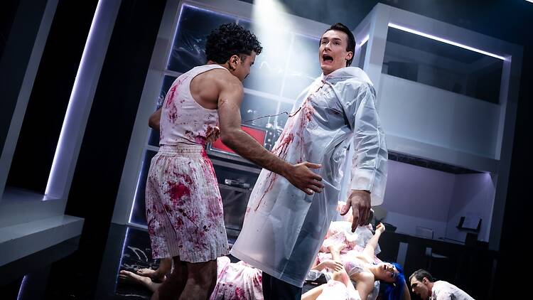 American Psycho – The Musical Two men in blood splattered clothing and bodies in the background.