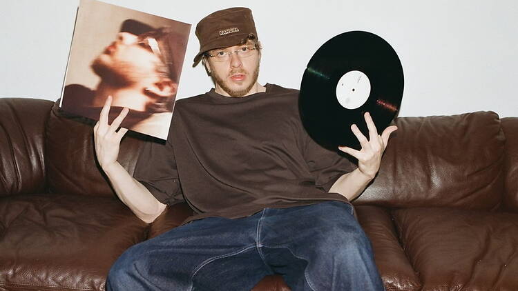 A wide shot of a person sitting on a couch holding a vinyl record and album cover indoors A wide shot of a person sitting on a couch holding a vinyl record and album cover indoors