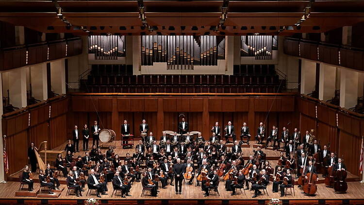 A wide shot of an orchestra performing on a concert hall stage. A wide shot of an orchestra performing on a concert hall stage.