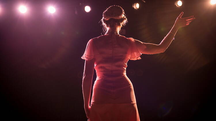 A wide shot of a person raising an arm on a stage under bright lights. A wide shot of a person raising an arm on a stage under bright lights.