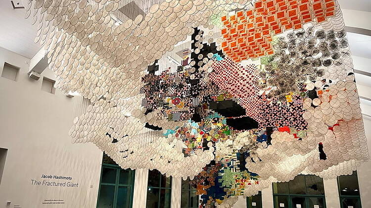 A wide shot of a suspended art installation displayed inside a museum gallery. A wide shot of a suspended art installation displayed inside a museum gallery.