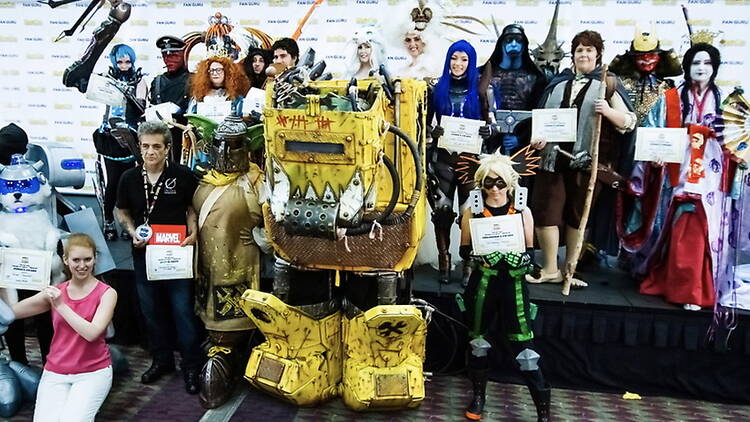 A wide shot of costumed participants posing together on a convention stage. A wide shot of costumed participants posing together on a convention stage.