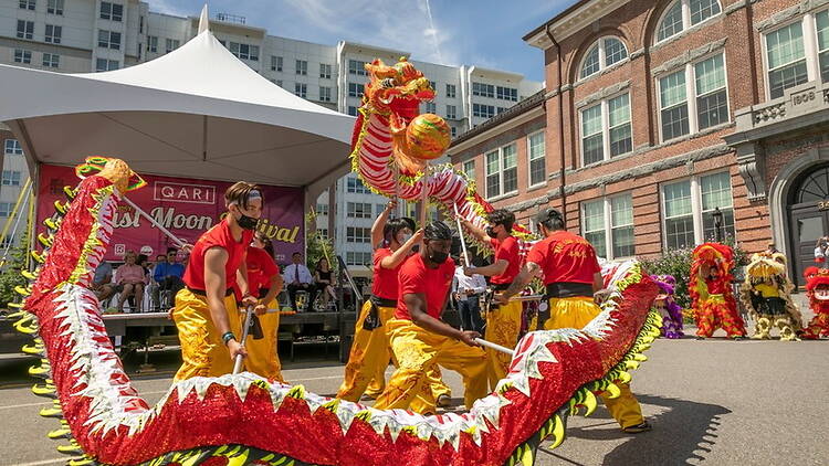 A wide shot of performers dancing with a dragon during an outdoor festival. A wide shot of performers dancing with a dragon during an outdoor festival.