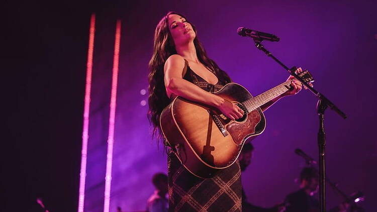 A wide shot of a musician playing an acoustic guitar on a concert stage. A wide shot of a musician playing an acoustic guitar on a concert stage.