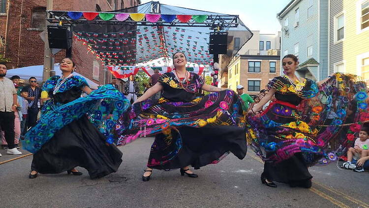 A wide shot of dancers performing in colorful dresses during a street festival. A wide shot of dancers performing in colorful dresses during a street festival.