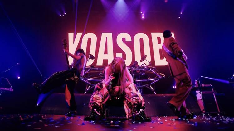 A wide shot of a band performing on stage under purple lights at a live concert. A wide shot of a band performing on stage under purple lights at a live concert.