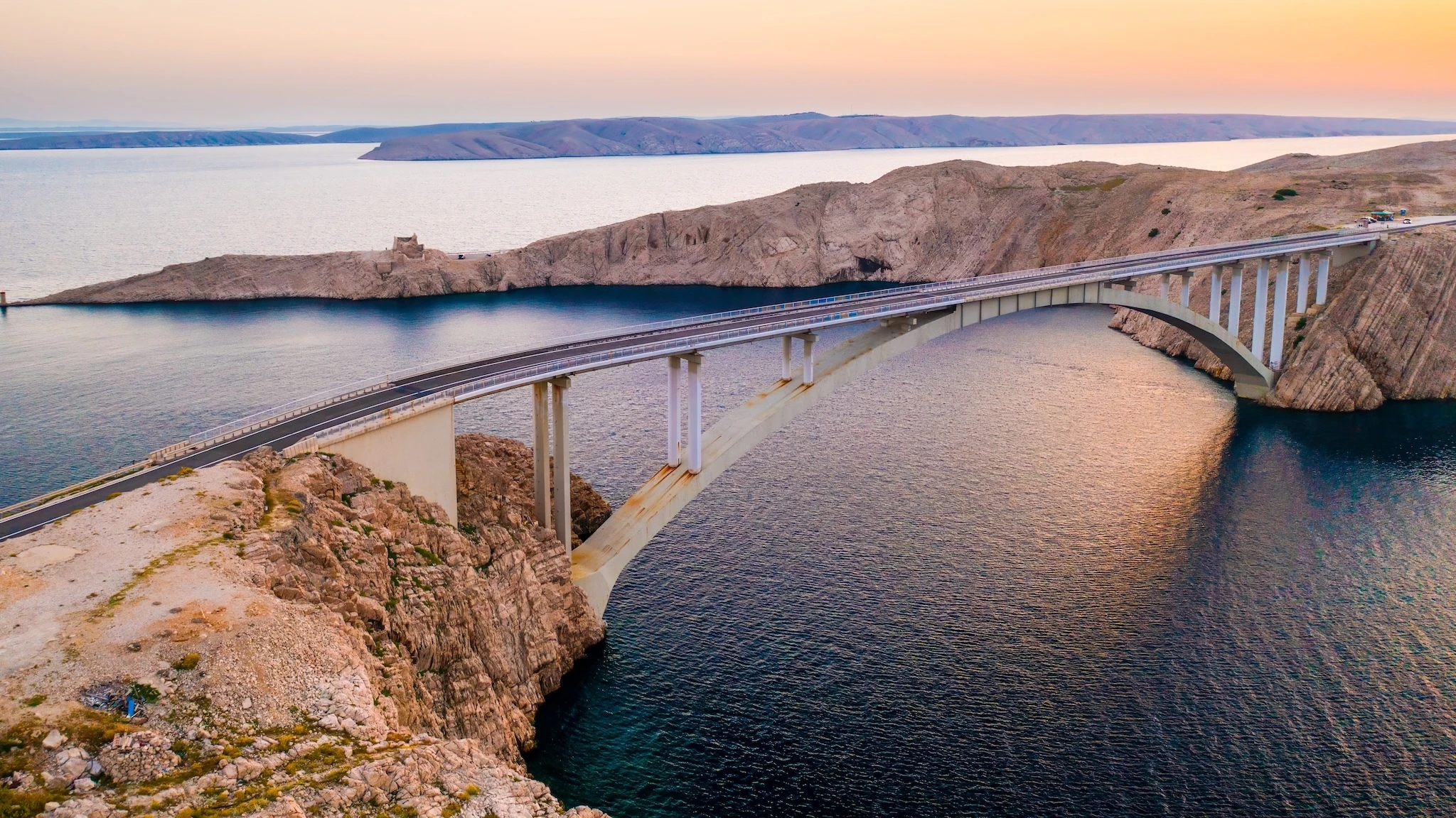 Pag Bridge with driving vehicles over Adriatic Sea channel at sunset