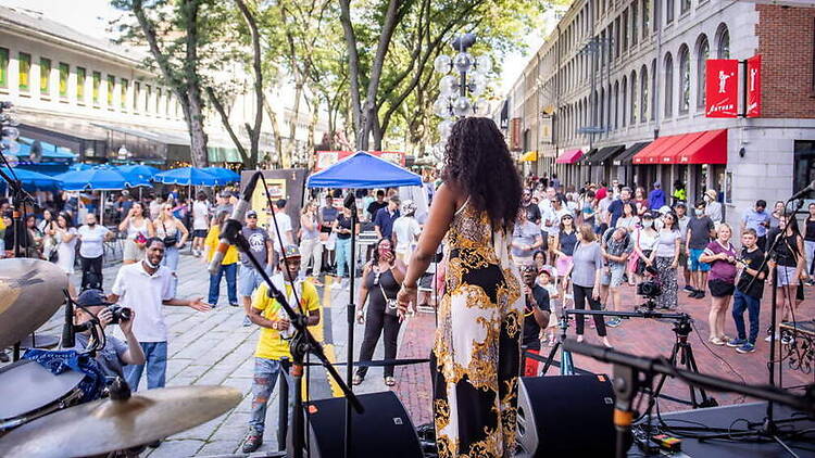 A wide shot of a singer performing on an outdoor stage before a crowd at a street festival. A wide shot of a singer performing on an outdoor stage before a crowd at a street festival.