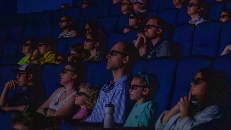 A wide shot of people watching a movie in a dark theater. A wide shot of people watching a movie in a dark theater.