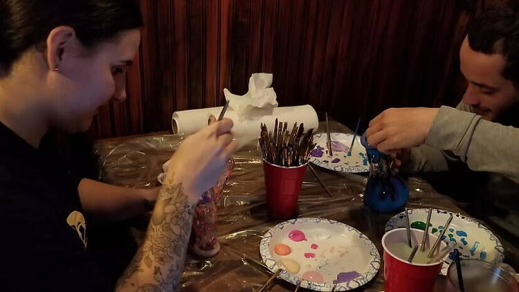 A close-up of people painting pottery at a craft workshop. A close-up of people painting pottery at a craft workshop.