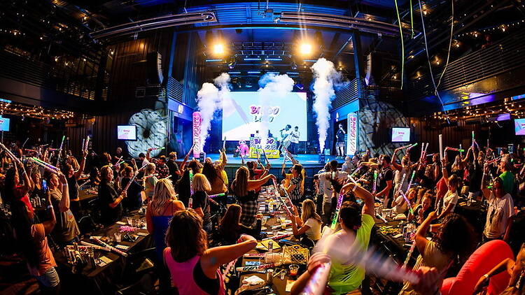 A wide shot of attendees cheering with inflatable sticks at a bingo event in a large indoor venue.