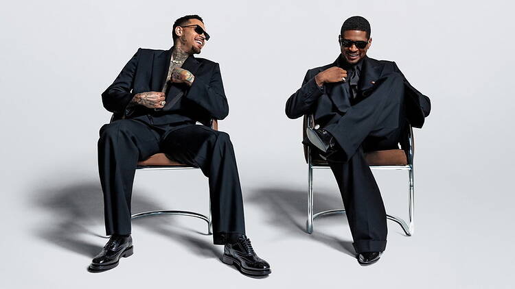 A wide shot of two men laughing while seated on chairs in a photo studio. A wide shot of two men laughing while seated on chairs in a photo studio.